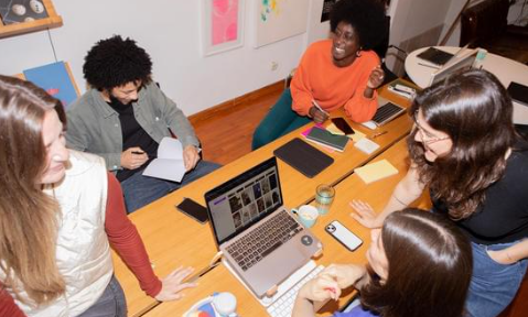 Eine Gruppe von jungen Erwachsenen sitzt fröhlich um einen Laptop zusammen